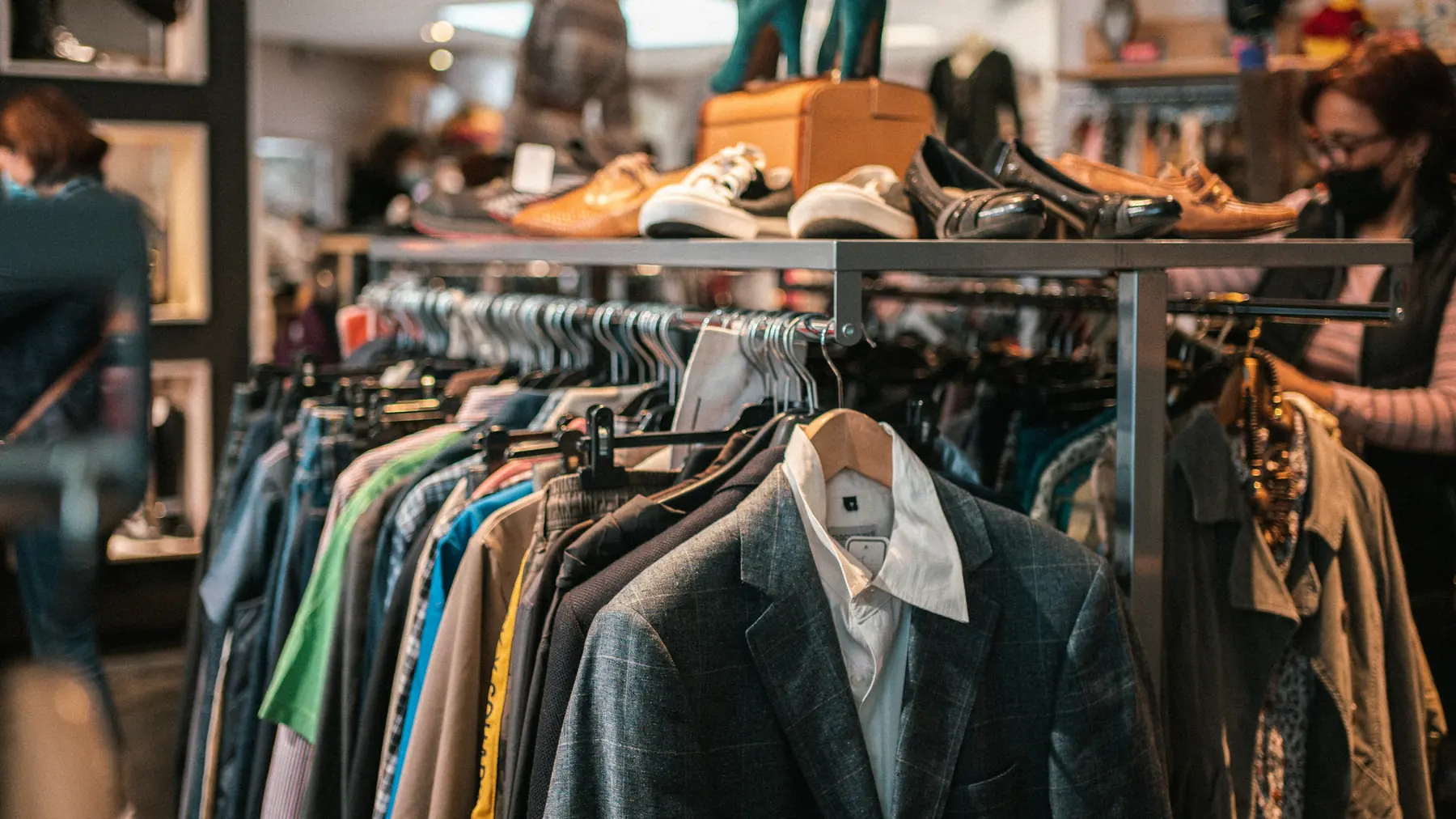 Racks of secondhand jackets and shirts with shoes displayed above