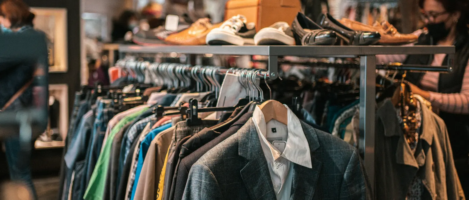Racks of secondhand jackets and shirts with shoes displayed above